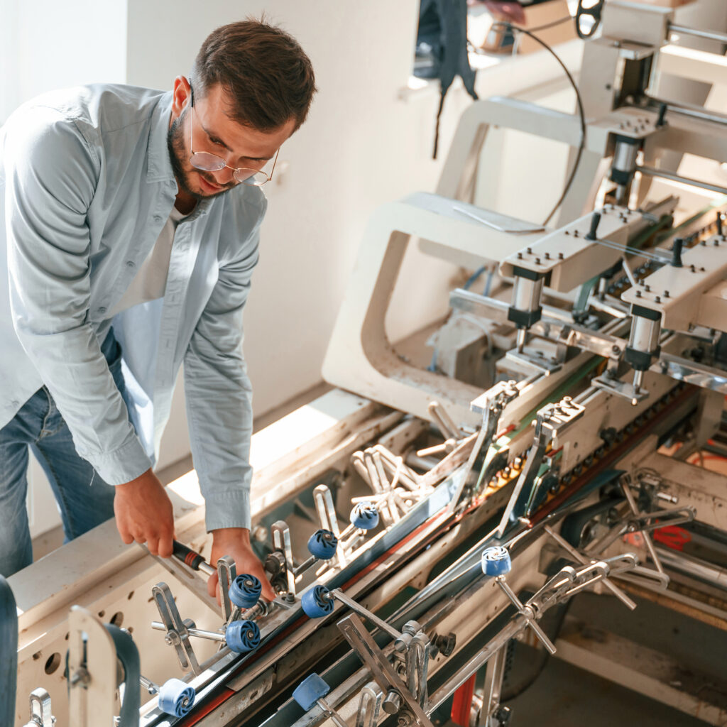 Setting up a printing machine. Typography worker in white clothes is indoors.